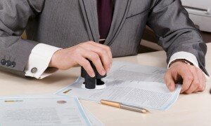 A person at a desk using a stamp or corporate seal on documents